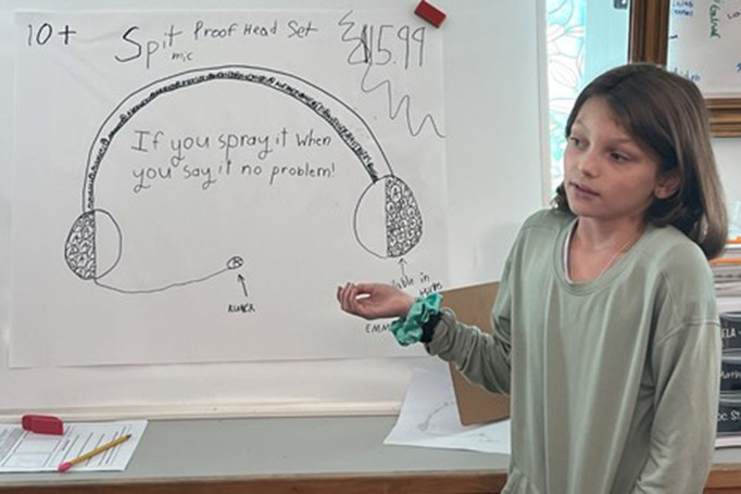 Close up of young child presenting an illustration of a headset on a poster board
