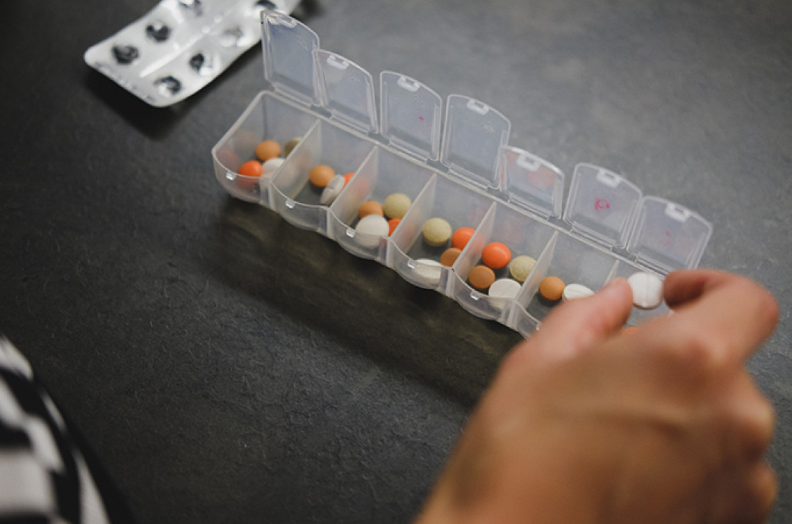 A hand organizes medical pills from their package into a weekly personal pill organizer