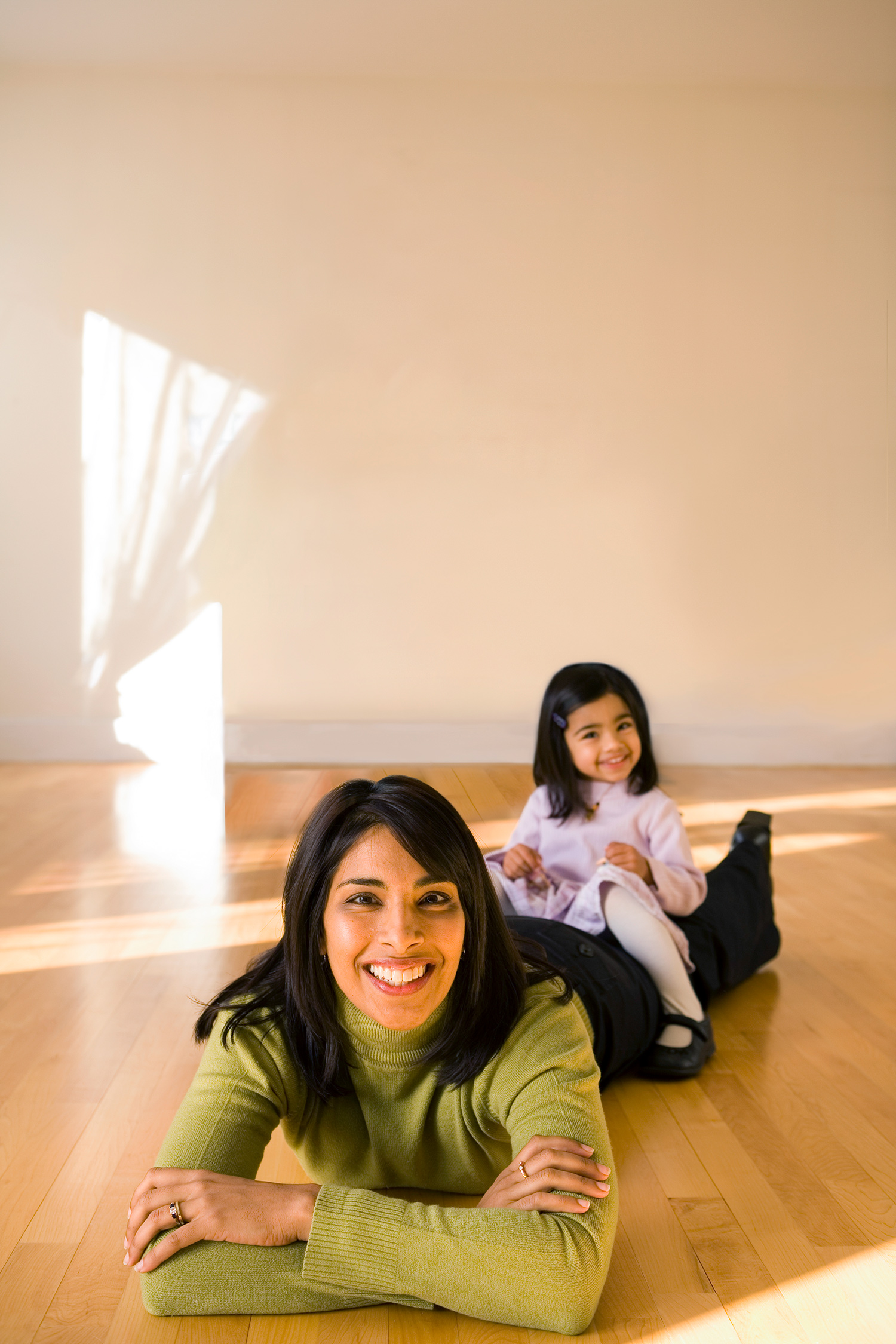 Sangeeta Bhatia lies on a wooden floor and is propped up on her elbows. Her daughter sits on her legs.