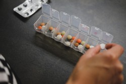 一只手将药丸从包装中整理成一个每周的个人药丸管理器