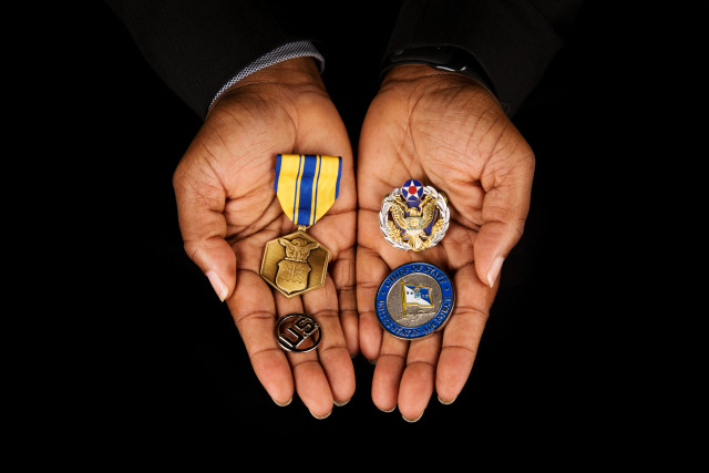 hands holding Air Force Commendation Medal, U.S. insignia, Challenge Coin from General John Jumper (Air Force Chief of Staff), and Headquarters Air Force Badge.