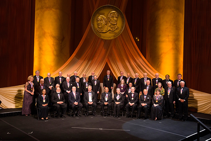 All present NIHF inductees sit or stand on stage for a group photo at the 2018 NIHF induction ceremony. 