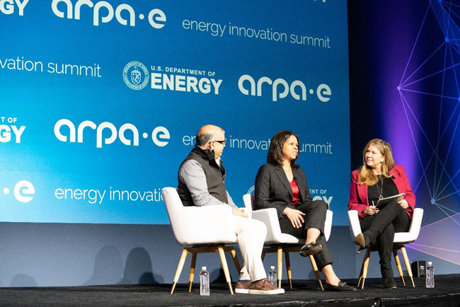 Kathi Vidal speaks on a conference stage, sitting with two other people, with logo for the ARPA-E energy innovation summit in the background