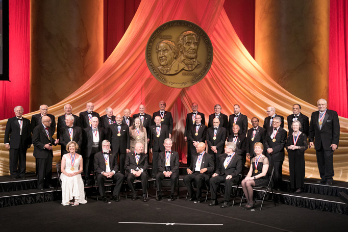 Men and women in black tie attire being honored on-stage under.