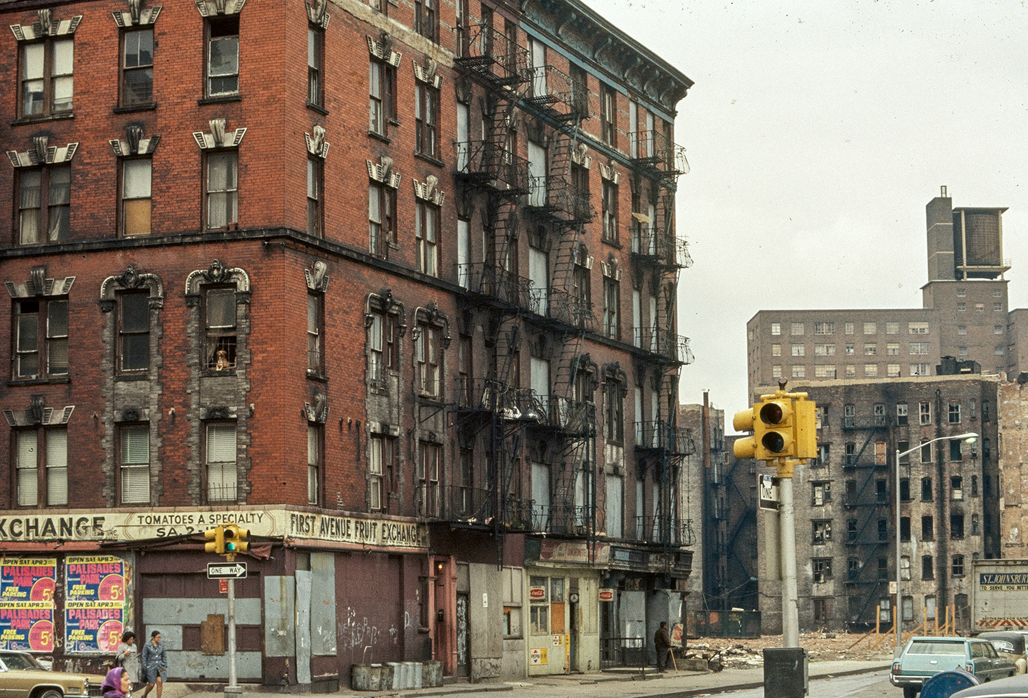 Corner view of a six-story tenement building in New York City with its storefronts boarded up.