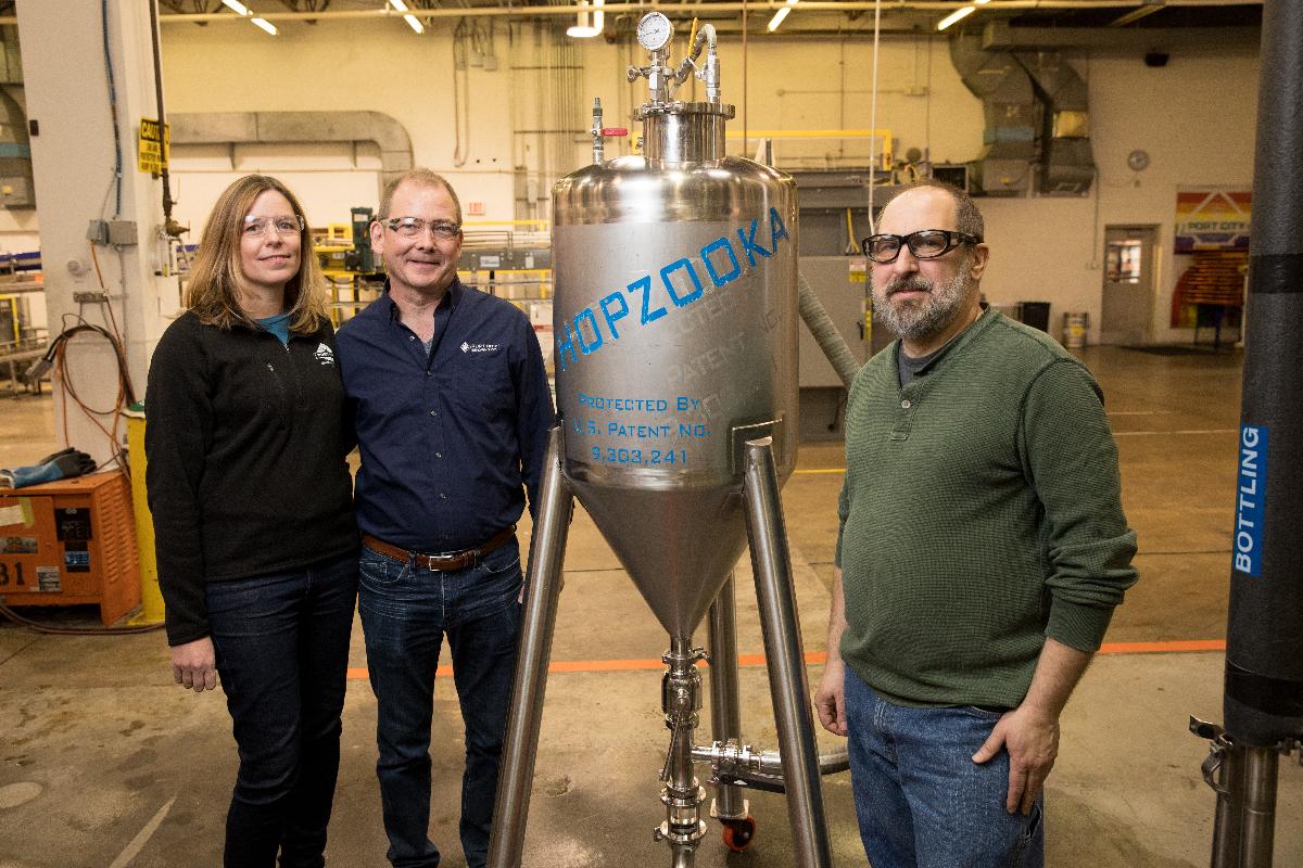 Image: Karen and Bill Butcher stand next to the patented Hopzooka ®, invented by head brewer Jonathan Reeves at right.