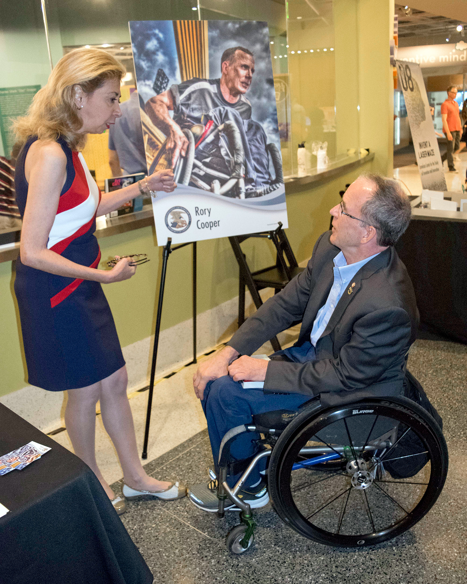 Deputy Director of the USPTO Laura Peter and Professor Rory Cooper(in wheelchair) with a blown up copy of his inventor trading card at his inventor trading card unveiling