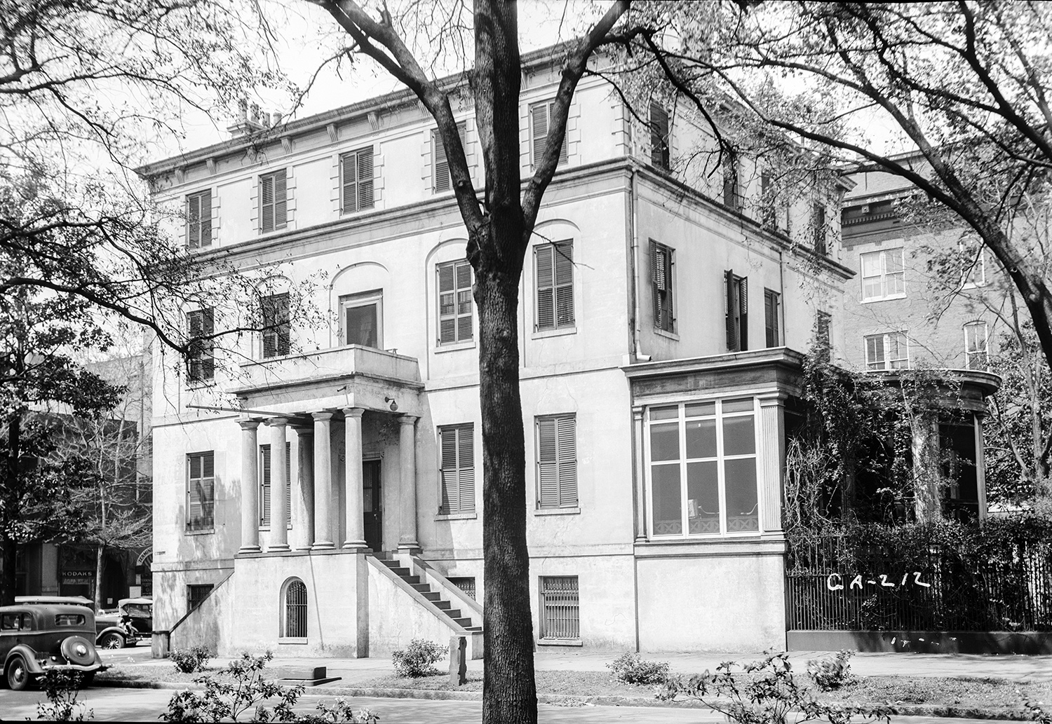 A stately, three-story home with a screened porch on the side and a columned, covered portico at the front. 