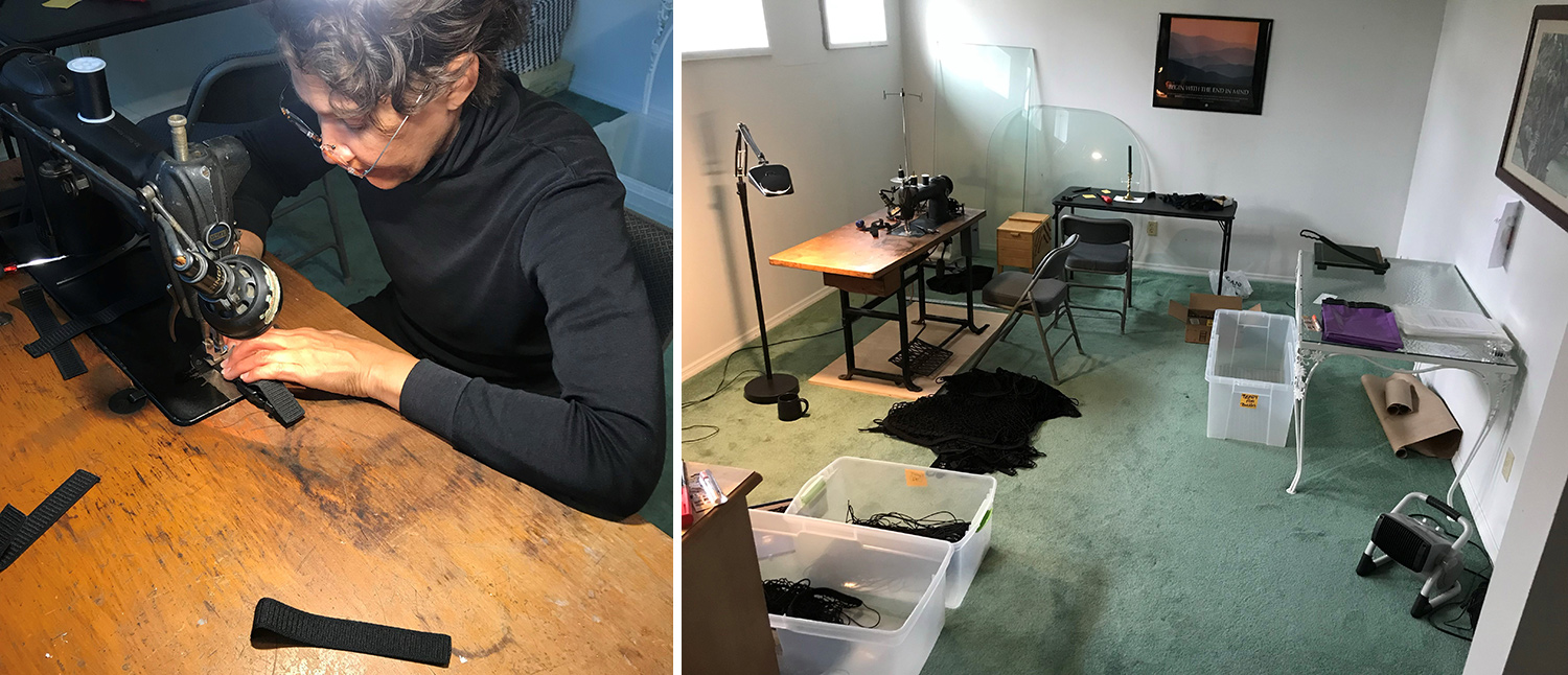 Woman in black long sleeve turtleneck with glasses sews loops with a black vintage sewing machine on a brown wood sewing table.   A room with light green carpet and white walls with bins of equipment and workstation tables.