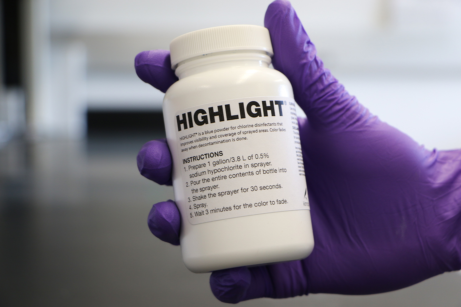 A gloved hand holds a bottle of Highlight.
