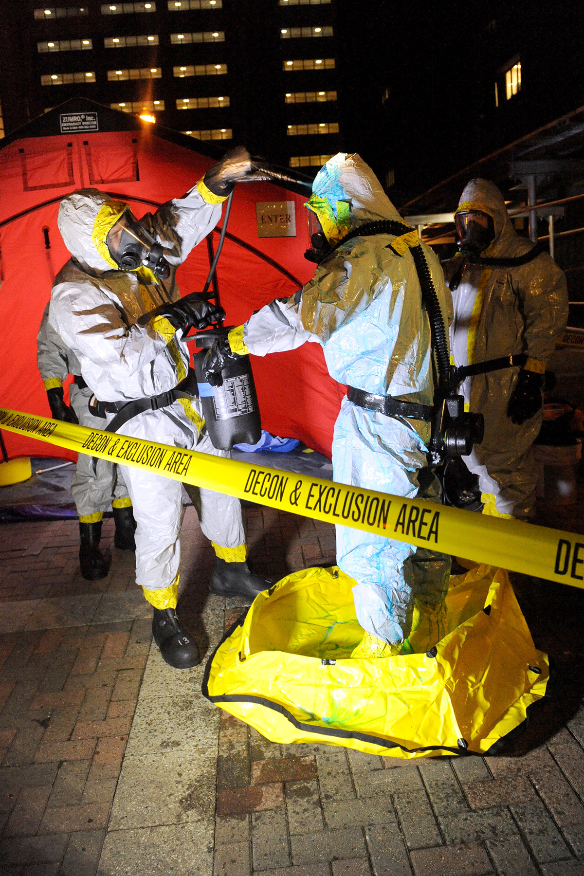 A healthcare worker is spraying another worker in a hazmat suit with bleach that includes Highlight.