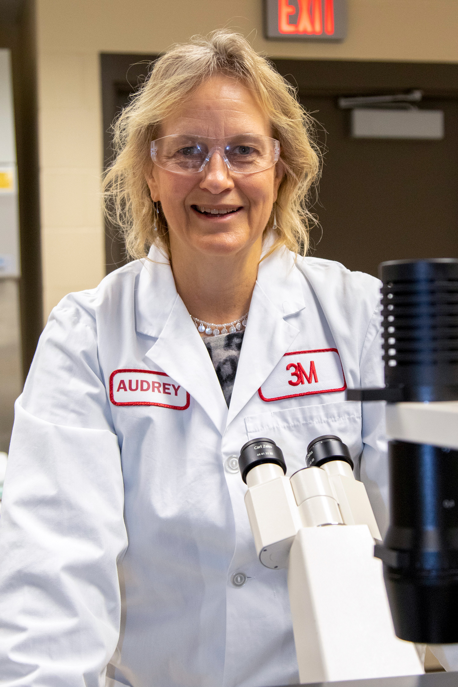In her lab coat, Audrey Sherman stands behind a microscope.