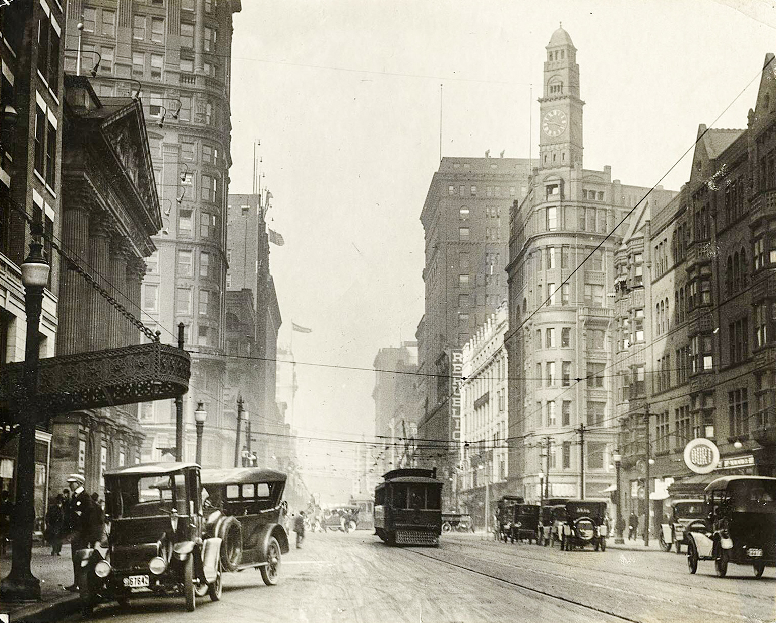 A city street packed with vehicles, streetcars, pedestrians, and a horse and buggy, surrounded by high-rise buildings