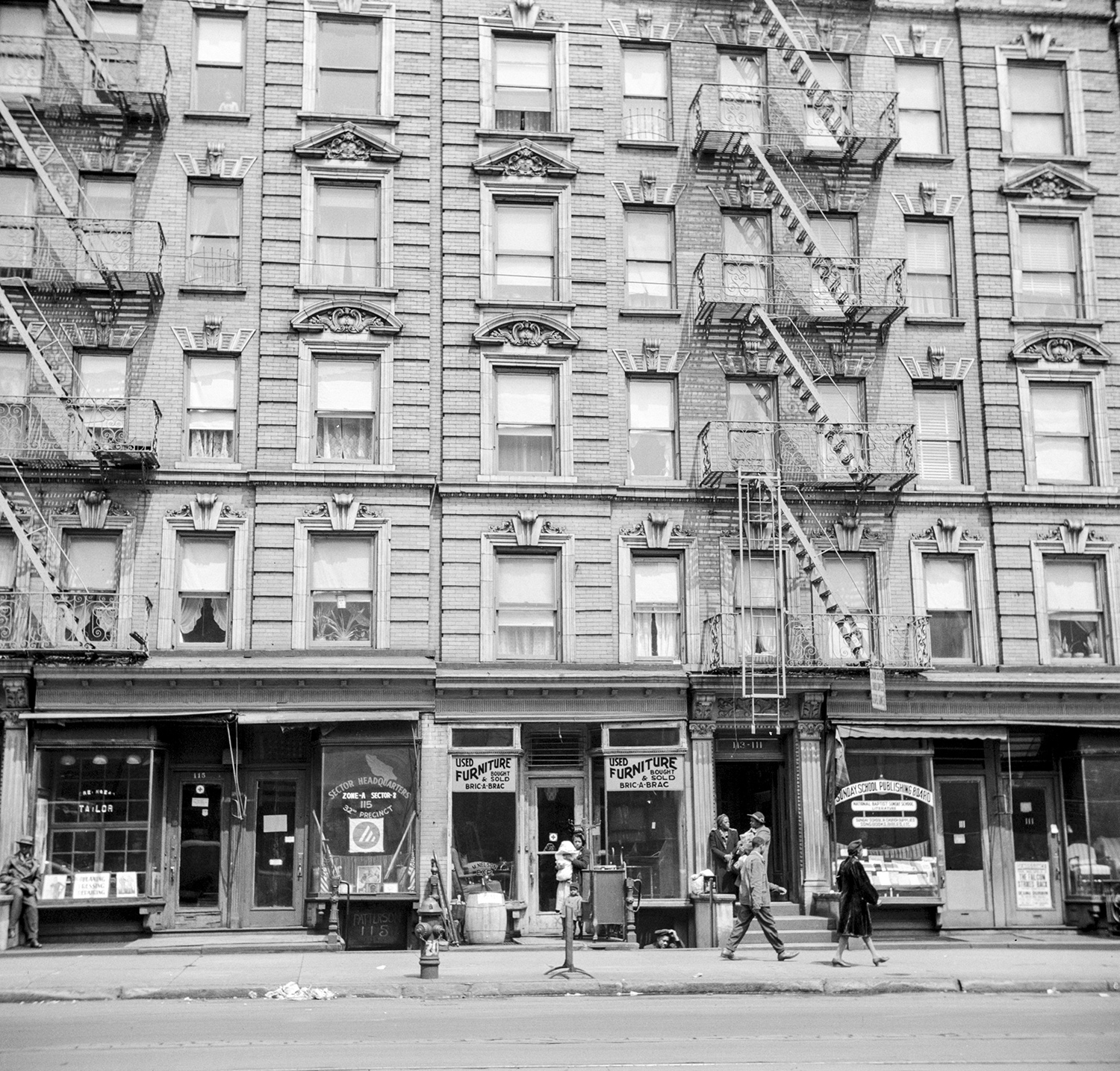 A 1940s photograph of two five-story tenement buildings with fire escapes and shops at street level. 