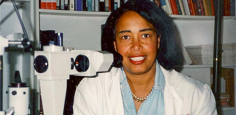 In a white lab coat, Dr. Patricia Bath smiles into the camera. 