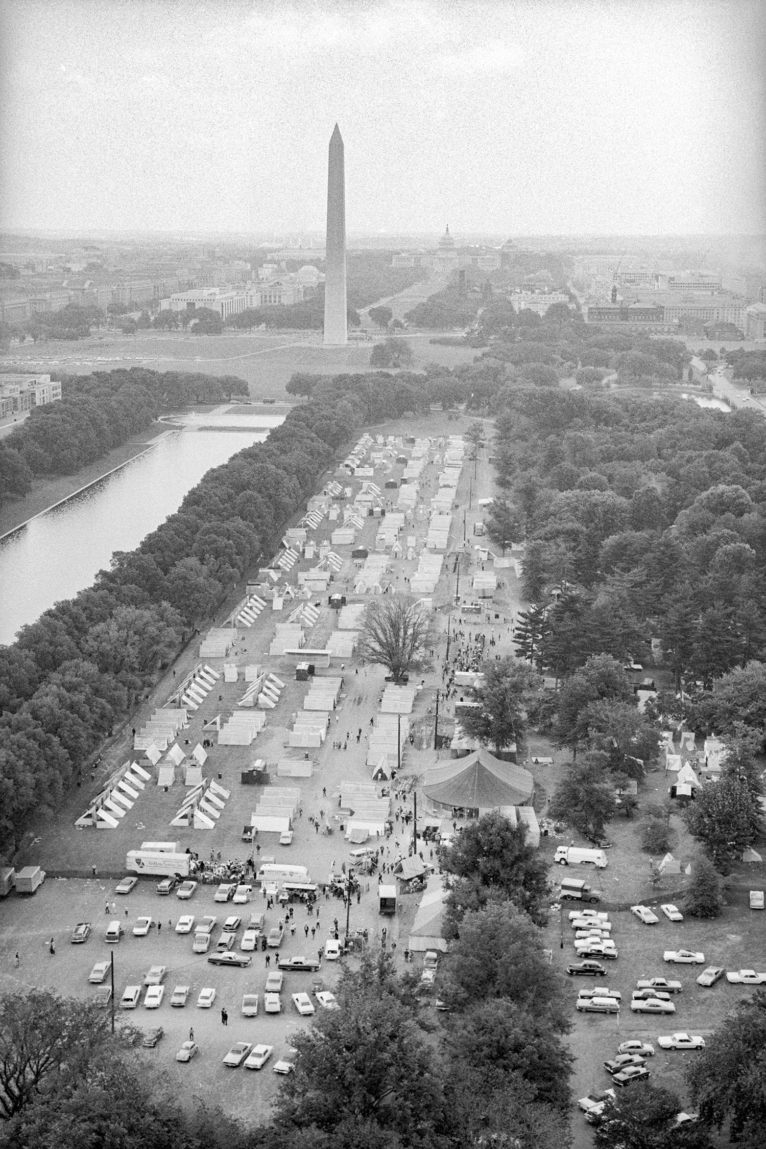 An aerial view of the National Mall in Washington, DC, covered in rows of tents, with the Washington Monument visible in the background. 
