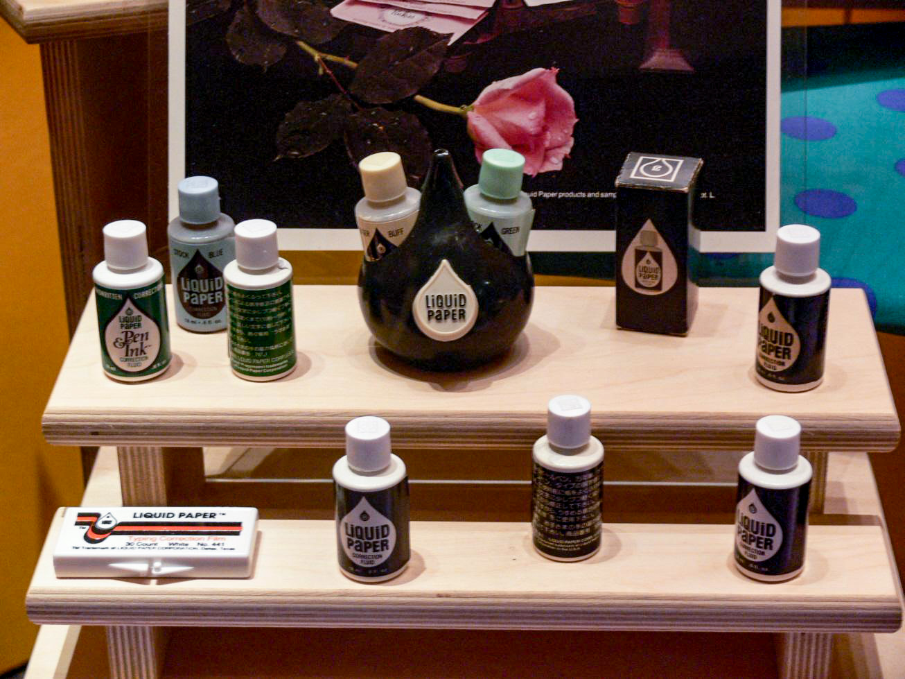 A colored photograph of a museum display showing several small bottles of Liquid Paper correction fluid in various colors.
