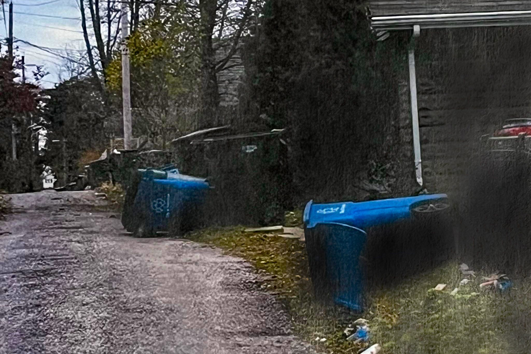 Residential garbage cans shown overturned in a small neighborhood alleyway.