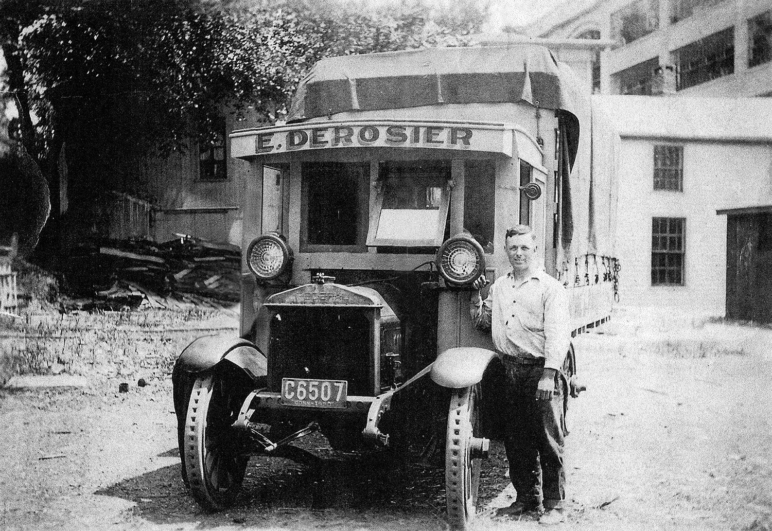 Old photo from the early 1900s with a man standing next to a period truck