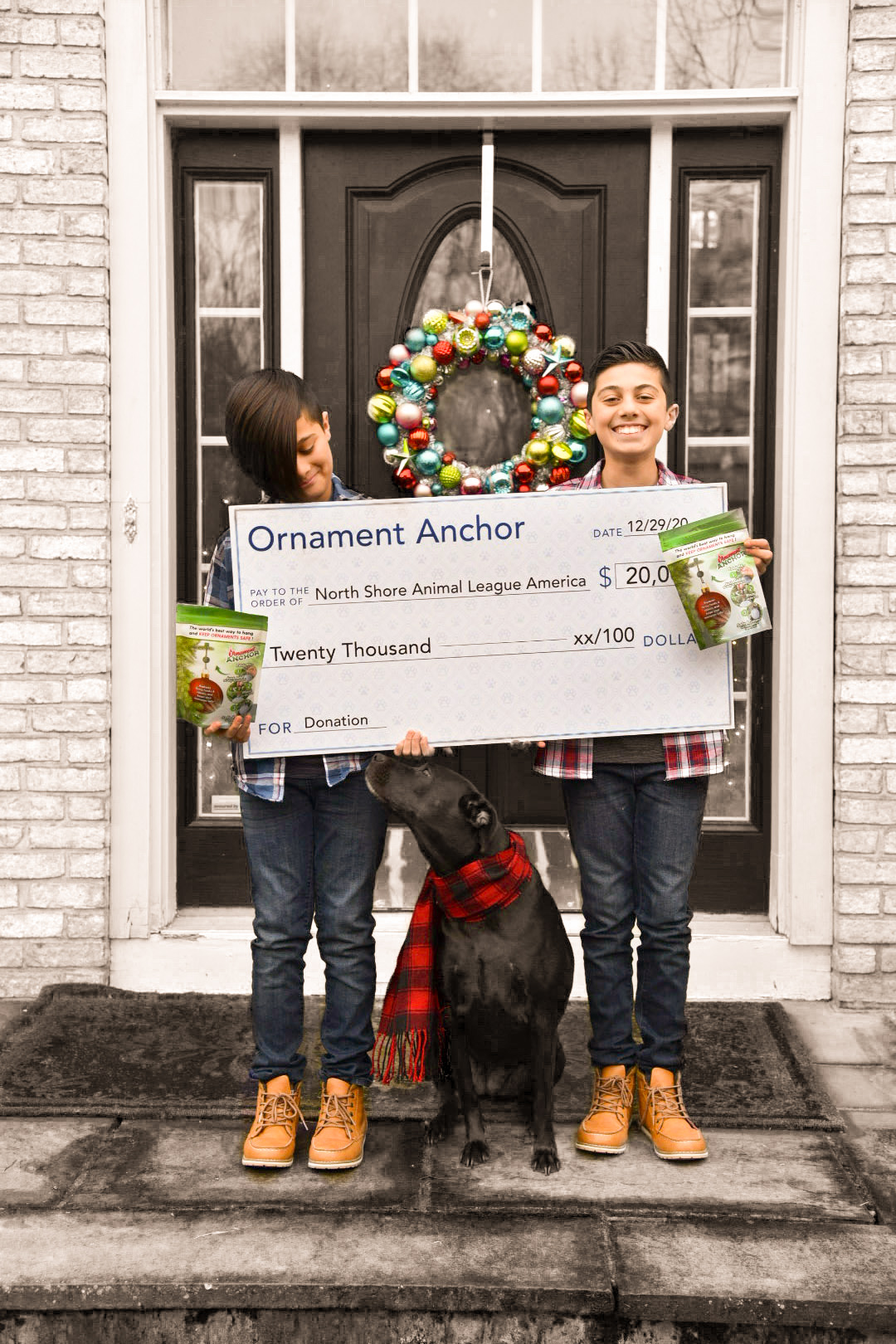 Two boys hold a big check in front of a door with a dog sitting in the middle of them