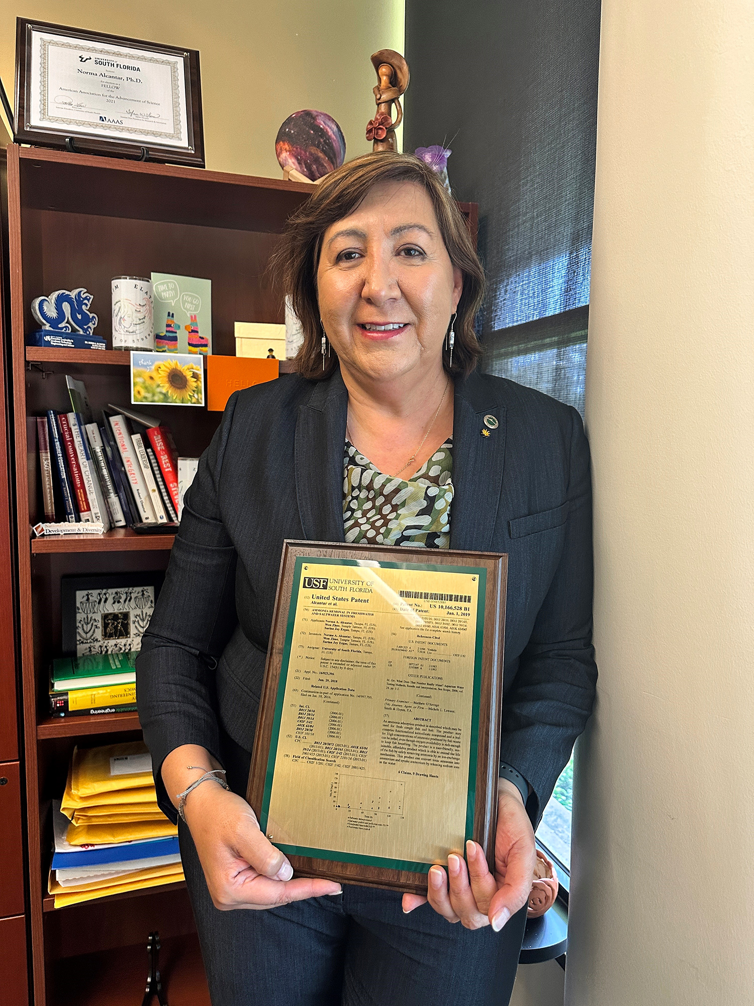 Smiling female inventor holding patent drawing plaque in office