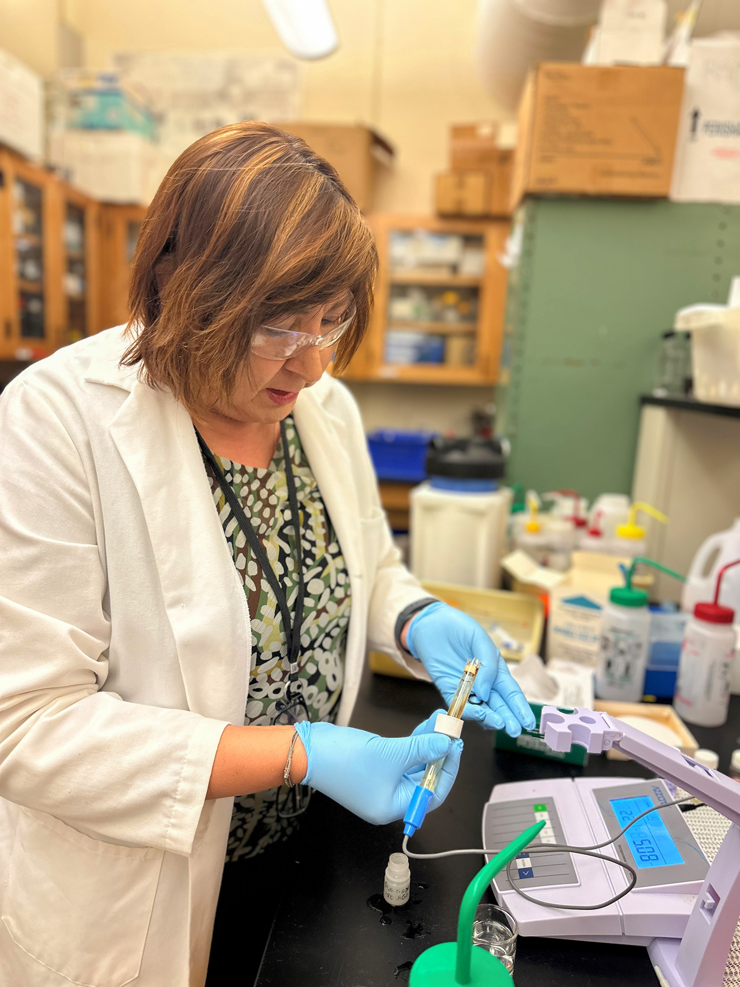 Una profesora universitaria con una bata de laboratorio blanca y guantes prueba los niveles de PH del agua utilizando equipo científico.