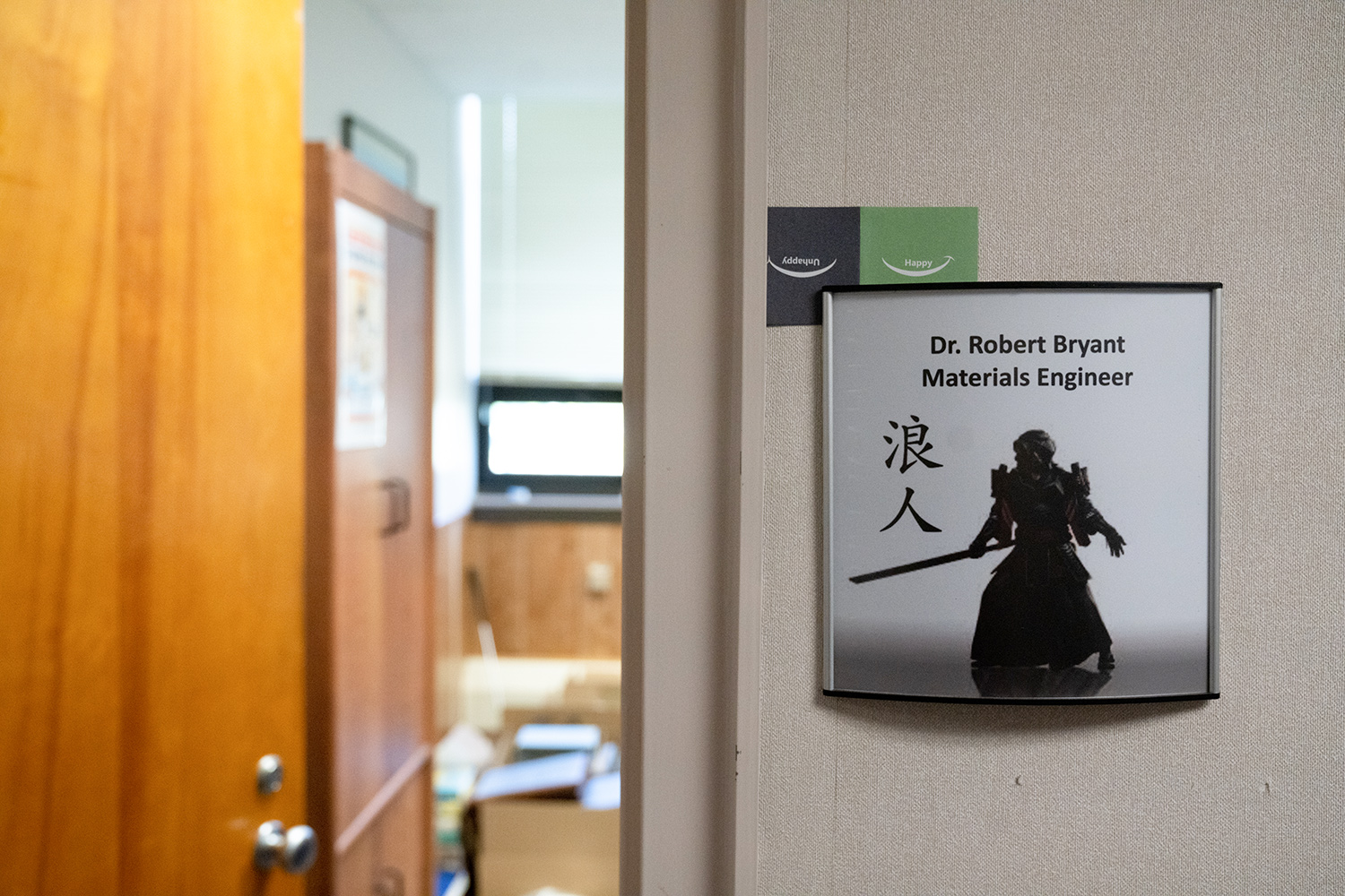 Dr. Robert Bryant’s office sign featuring his name, an illustration of a silhouetted ronin, and Japanese characters with his office door open and a slight view of the boxes inside
