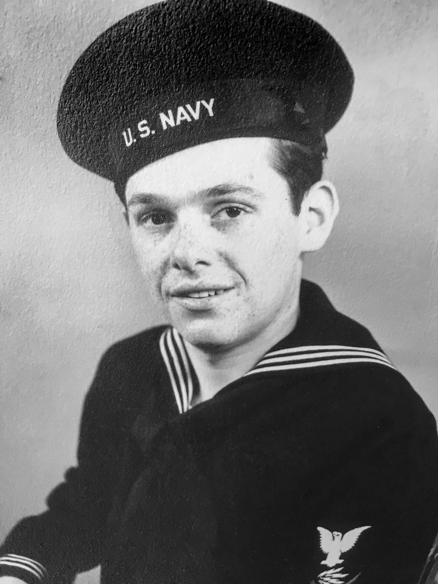 A young male sailor wearing the United States Navy’s winter uniform and cap smiles. 
