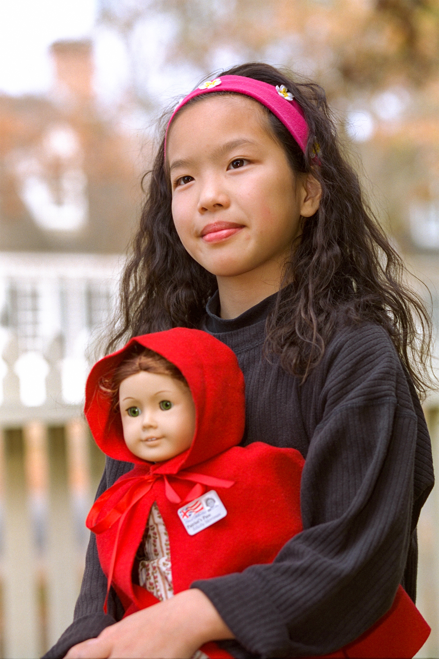 A young Asian-American girl visits Colonial Williamsburg cradling a Felicity Merriman doll. Pinned to the doll’s red cloak is a miniature Colonial Williamsburg visitor badge. 