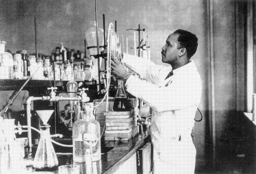 A man in a white coat works with equipment in a laboratory.