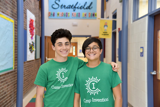 Two young teenagers wearing Camp Invention t-shirts in a school hallway