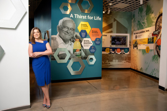 Woman in blue dress stands in front of a museum display of Gatorade inventor