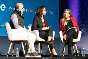Kathi Vidal sitting on a stage discussing a topic with a male and female speaker.