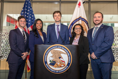 PTAB FY22 judicial law clerks Patric R., Safiya A., Keaton S., Isha S., and Drew N. standing behind a podium with the seal of the United States Patent and Trademark Office.