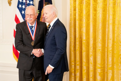 Charles Hill wearing a dark suit and glasses, shakes President Biden’s hand, right after receiving the National Medal of Technology and Innovation.