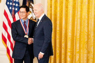 Kim Jeong wearing a dark suit and glasses, shakes President Biden’s hand, right after receiving the National Medal of Technology and Innovation.