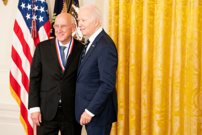 Steve Rosenberg wearing a dark suit and glasses stands with President Biden, after receiving the National Medal of Technology and Innovation.