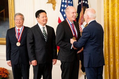 James Fujimoto, David Huang, and Eric Swanson (L-R), all dressed in dark suits with Fujimoto wearing glasses, receive the National Medal of Technology and Innovation from President Biden, as a team.