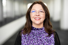 Headshot of USPTO patent examiner Ana Muresan. She wears glasses and a purple and black top and is smiling.