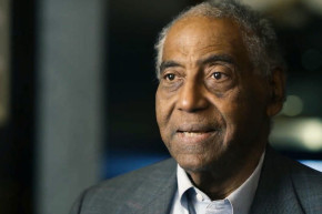 An older African American man in a suit jacket speaks during an interview 