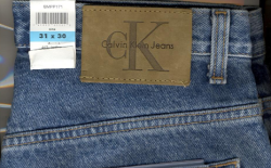 Close-up photo of a leather patch on the back of a denim waistband. The patch is tan and branded with a Calvin Klein trademark.