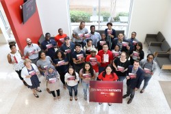 A diverse group of people standing, looking up, and holding postcards saying “ten million patents” with Hope Shimabuku, the director of the Texas regional office of the USPTO, standing in the front row and holding a large sign saying “ten million patents”