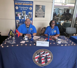 Clifton R. and Angela J. sit at the USPTO Military Association table during a Women in IP event March 2024.