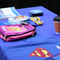 Photo of a vendor table displaying Superman T-shirts with two men and a woman engaged in a coversation.